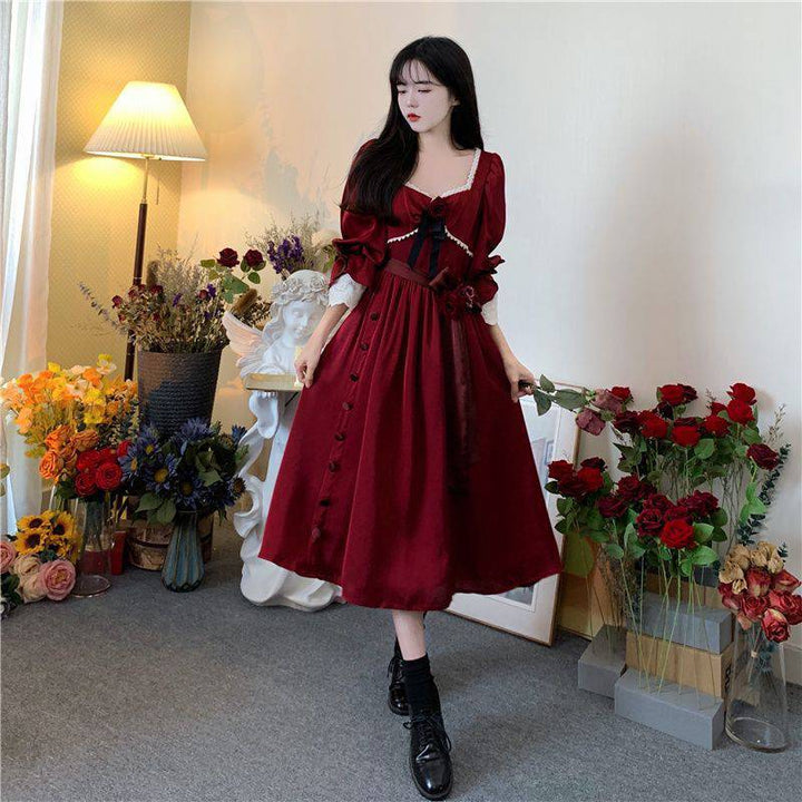 A woman in a Maramalive™ Velveteen Gothic Red-Rose Dress: Vintage Wine-Red Frock standing in front of flowers.