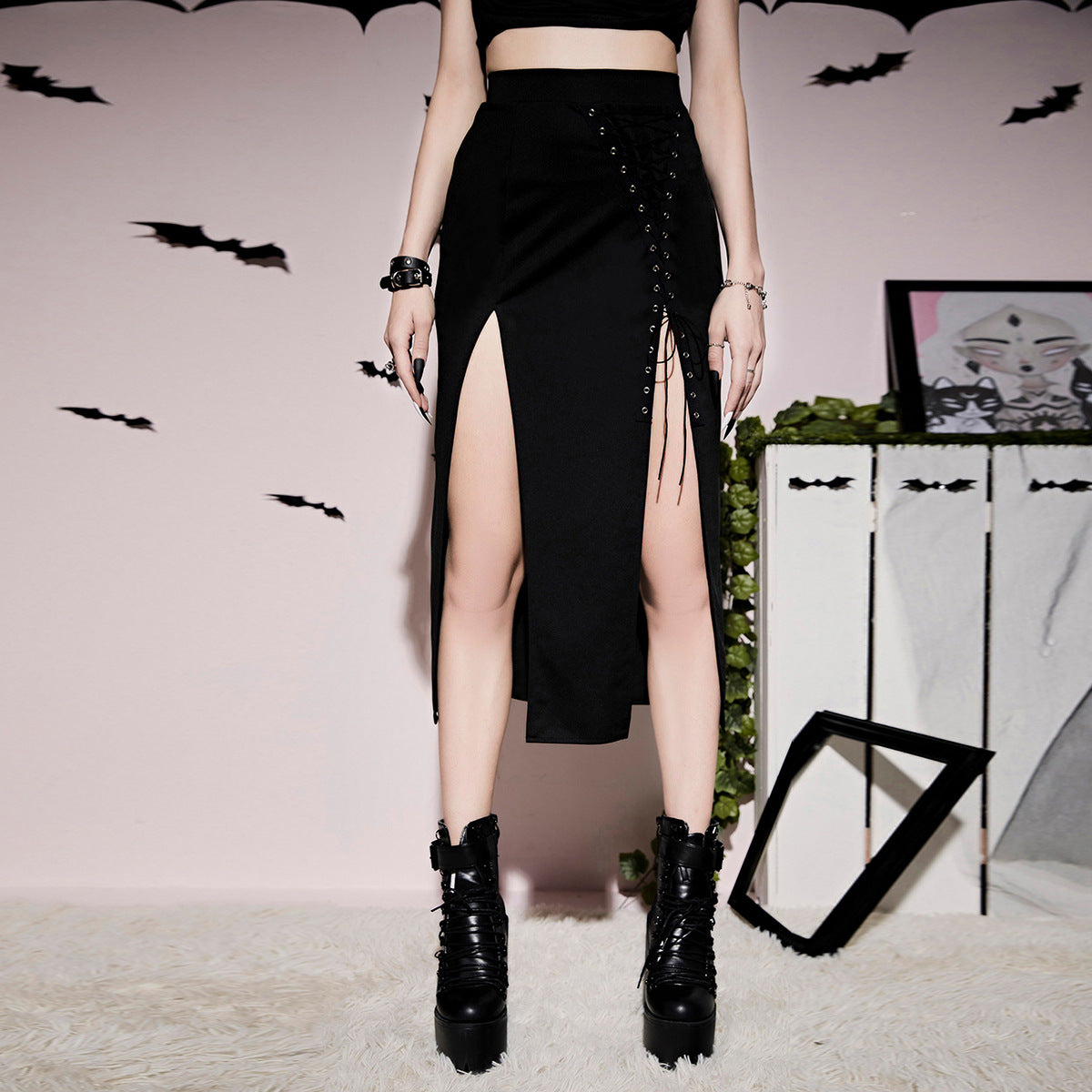 A woman in a Maramalive™ Gothic Style Lacing Half Skirt with thigh splits posing in front of a wall with bats.