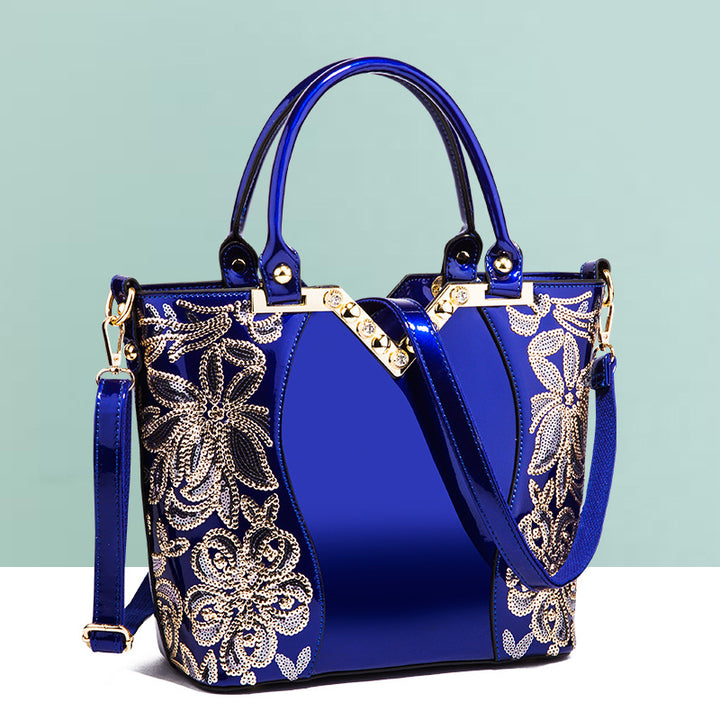 A shiny patent leather shoulder bag in blue with a floral design and zipper closure by Maramalive™.