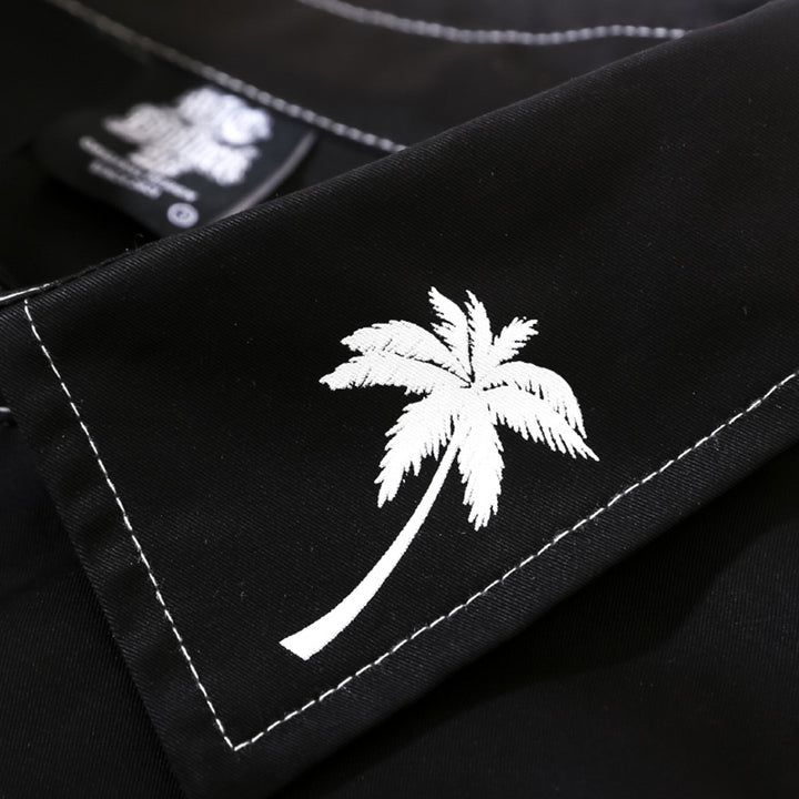 Close-up of a black garment with white stitching, featuring a white palm tree graphic on the fabric. The printed design showcases elegance and style, making this Maramalive™ men's printed long-sleeve shirt a versatile shirt for any occasion. A partially visible label is seen in the background.