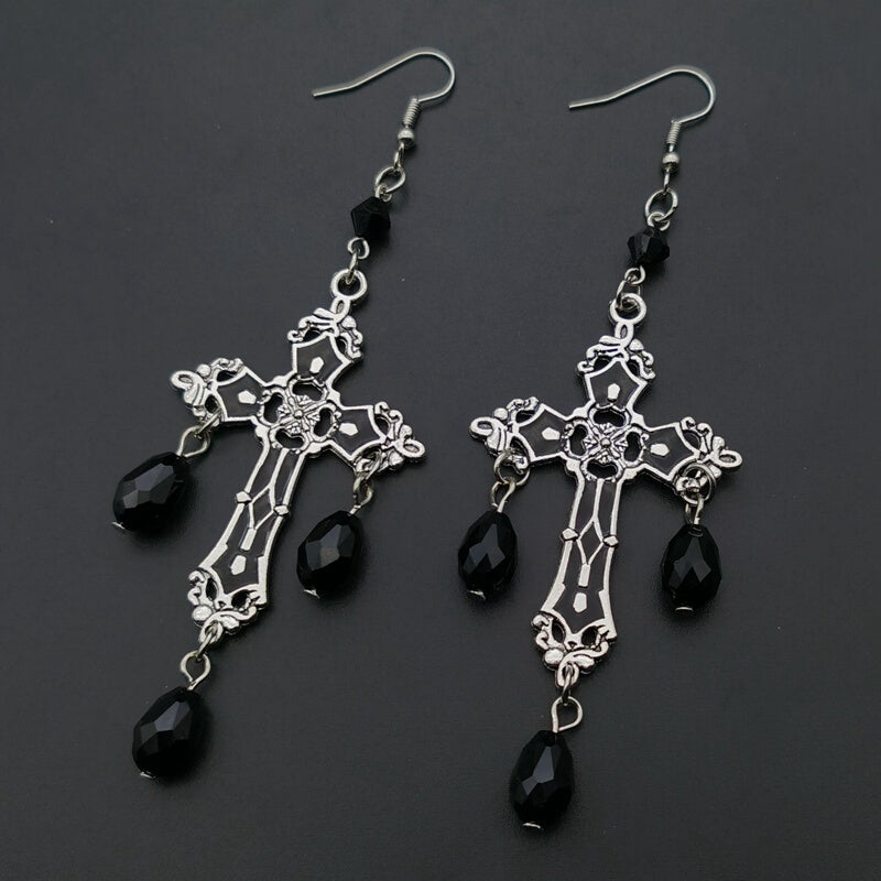 A pair of Gothic Black Cross Garnet And Crystal Chandelier Earrings La hanging from a person's hand, from the brand Maramalive™.