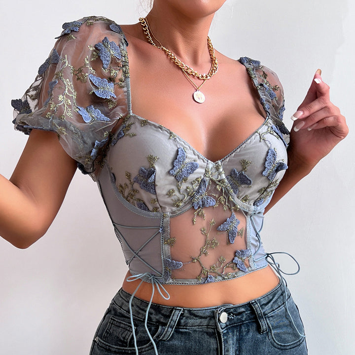 A person wearing a Maramalive™ Ladies New Hot Girl Backless See-through Camisole with floral embroidery and puffy sleeves, paired with jeans and a gold necklace with a pendant, epitomizes European and American style.