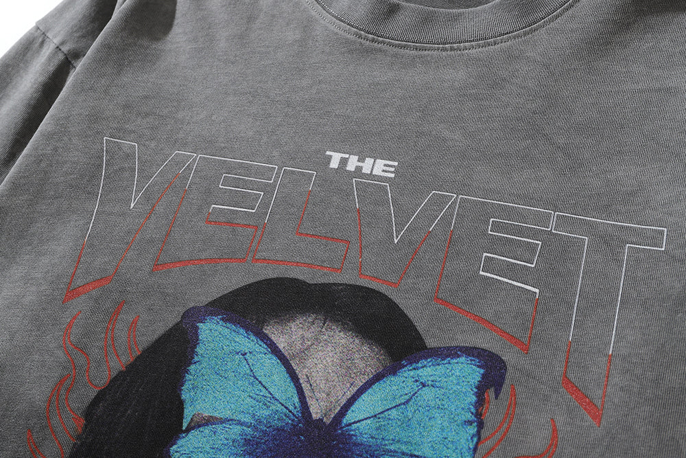 Close-up of a collarless gray Men's Dark Character Old Washed Long-sleeved T-shirt by Maramalive™ featuring the text "THE VELVET" in large, stylized font above a graphic of a blue butterfly over part of an obscured face.