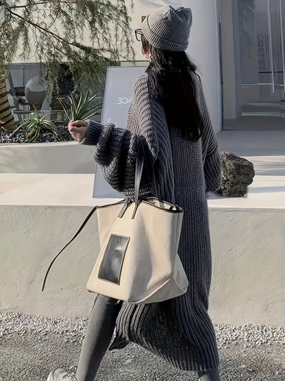 A person wearing a long gray V-neck Maramalive™ Plus Size Open Front Loose Knit Cardigan, Casual Long Sleeve Long Length Cardigan With Pocket, Women's Plus Size Clothing and a knit hat, carrying a beige tote bag, walks on a gravel path in front of a modern building.