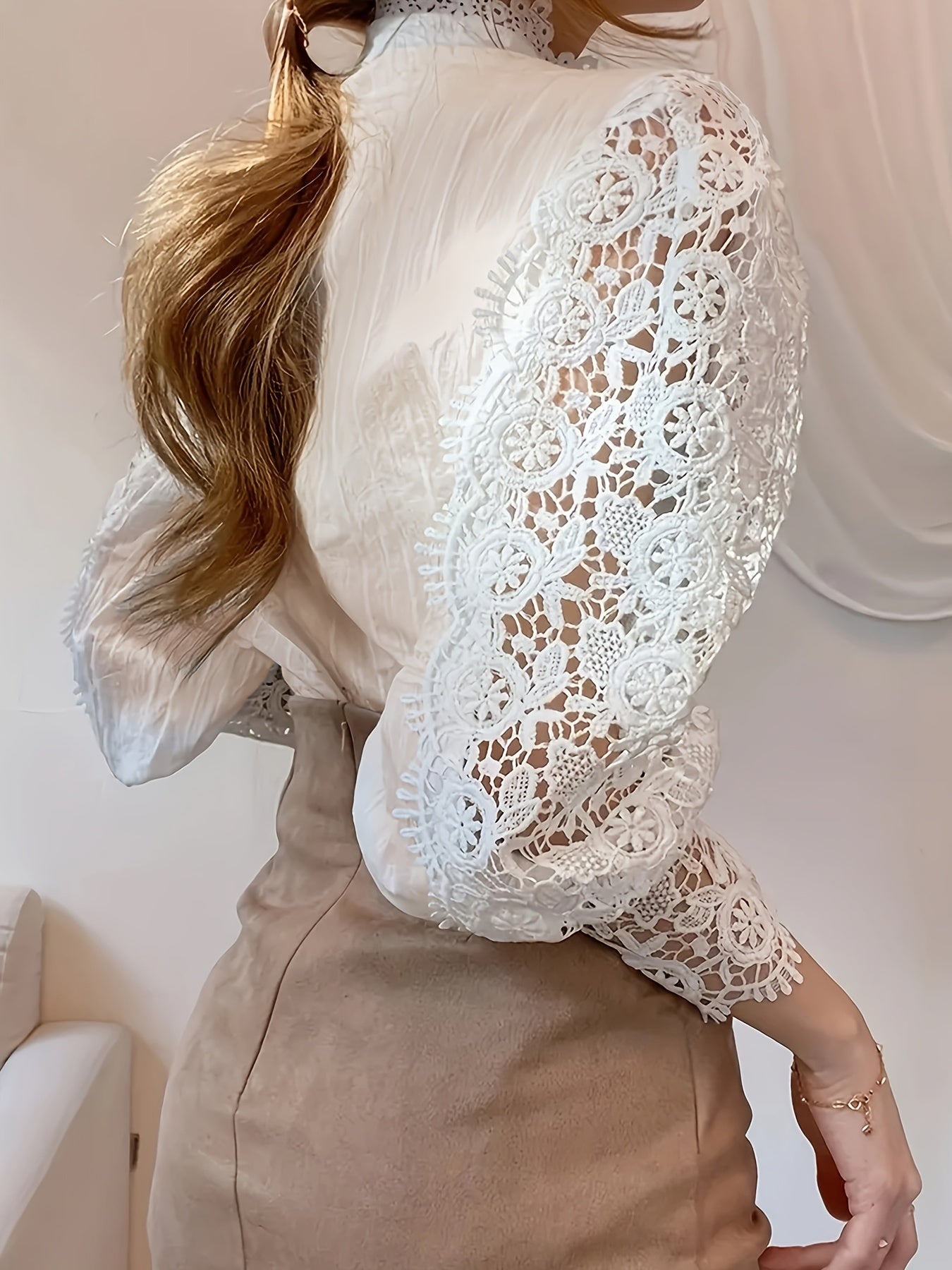 A person wearing a detailed white lace blouse with a mock neck collar and lantern sleeves, paired with a tan skirt. Their light brown wavy hair cascades over one shoulder, complementing the Maramalive™ Plus Size Elegant Blouse, Women's Plus Solid Contrast Lace Lantern Sleeve Button Up Mock Neck Shirt Top. The background appears to be a light-colored indoor setting.