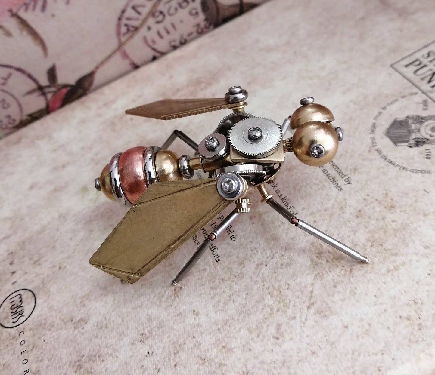 A Maramalive™ steampunk metal fly crafts sitting on top of a book.