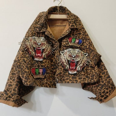 A Leopard Print Studded With Nails Bead Mesh Gauze Stitching Denim Short Coat Female with embroidered roaring tiger heads and crowns on the front, hanging on a hanger. Available in multiple size options. Brand Name: Maramalive™