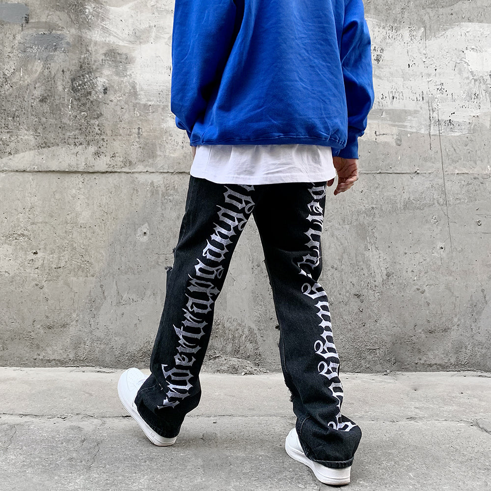 A man in Maramalive™ Hip Hop Vibe Back Gothic Alphabet Embroidery Ripped Micro Flared Denim Pants.