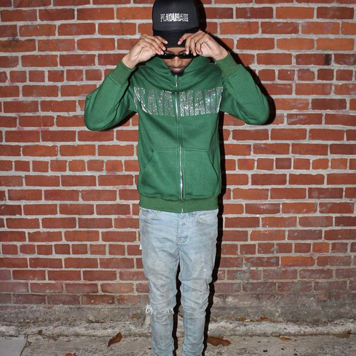 A street hipster wearing a Maramalive™ Letter New Long-sleeve Zipper Hoodie Fashion Casual Punk Coat Sweatshirt and light blue jeans stands against a brick wall, adjusting their black baseball cap and sunglasses.