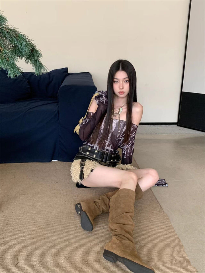 A woman with long hair sits on the floor beside a blue sofa, wearing Maramalive™ Off-shoulder Printed Mesh Long Sleeve Bottoming Shirt Sun Protection Shirt, beige shorts, and slim fit brown knee-high boots. She holds a black purse on her lap in an urban style setting.