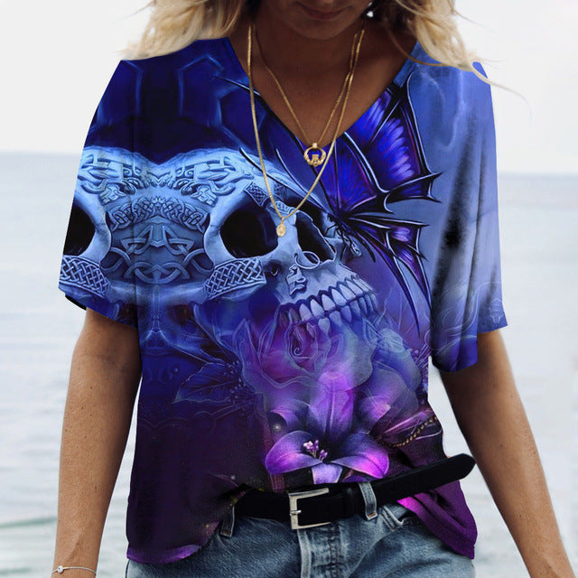 Person wearing a Maramalive™ Ladies' Printed V-Neck Tee | Chic Women's Graphic Tees with a flattering fit and vibrant fun prints featuring skulls and abstract elements, along with layered necklaces, standing in front of a blurred seascape background.