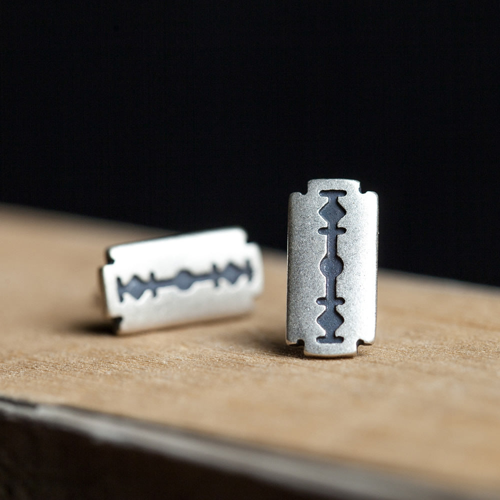 A pair of Refined Rebellion: Sterling Silver Razor Blade Gothic Ear Studs by Maramalive™ on a wooden table.