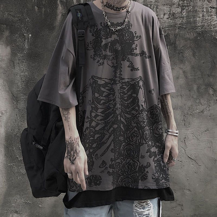 Person wearing a Maramalive™ Dark Hip Hop Tee - Perfect for Underground Rap Fans printed with a skeletal design and flowers, paired with distressed jeans and a backpack. The background is a rough, textured wall, embodying streetwear fashion.