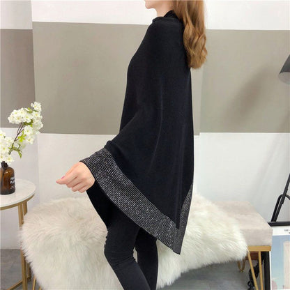 A person wearing a Maramalive™ Outer Bat Sweater With Diamond Studded Black Sweater stands in a modern, minimalistic room with a fur-covered bench and a small table with a vase of white flowers, exuding a simple commuting style.