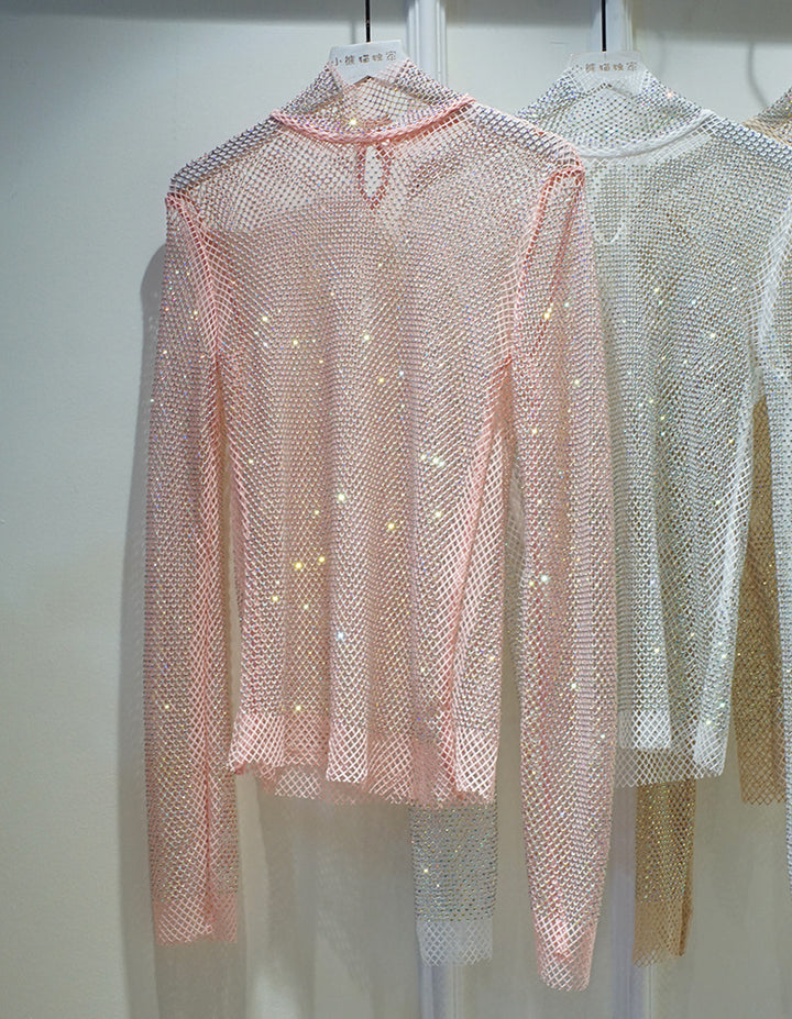 A sheer, long-sleeve, pink mesh top with a high collar design is displayed on a hanger. A light-colored lace shirt and a white top can be seen partially visible in the background. The New Crystal Rhinestone Hollow Top Starry Bright Sexy Ladies Long Sleeve See-through Net Diamond Shirt by Maramalive™ is elegantly showcased in the foreground.