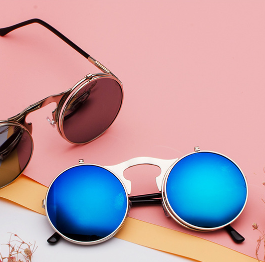 A pair of Maramalive™ Retro Metal Steampunk Flip Sunglasses Round Frame sitting on top of a pink surface.