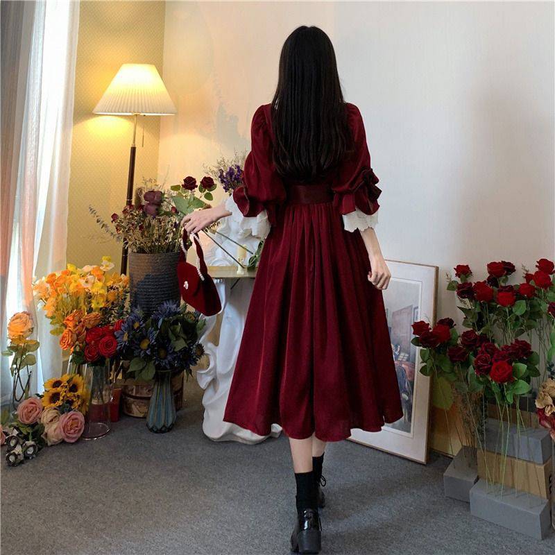 A woman in a Maramalive™ Velveteen Gothic Red-Rose Dress: Vintage Wine-Red Frock standing in front of flowers.