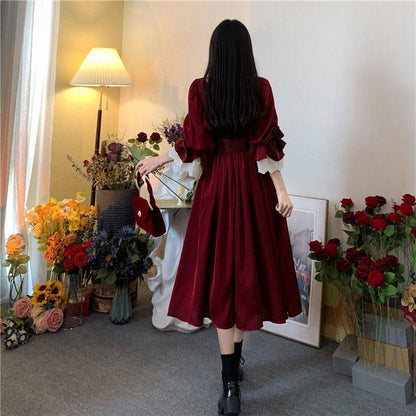 A woman in a Maramalive™ Velveteen Gothic Red-Rose Dress: Vintage Wine-Red Frock standing in front of flowers.