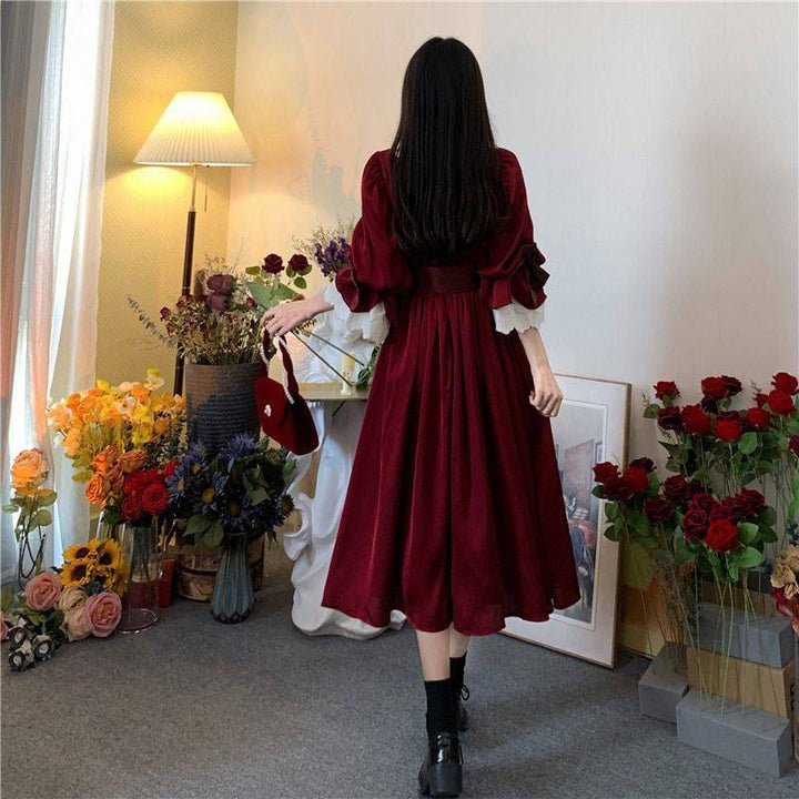 A woman in a Maramalive™ Velveteen Gothic Red-Rose Dress: Vintage Wine-Red Frock standing in front of flowers.