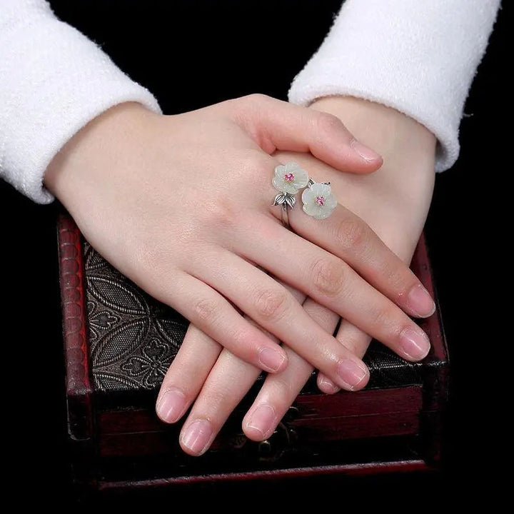 A Fashion Antique Flower Women's Ring by Maramalive™ with two white jade flowers on top of a wooden table.