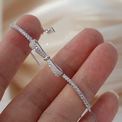 A woman's hand holding a Maramalive™ Minimalist Bow Pull Bracelet with diamonds.
