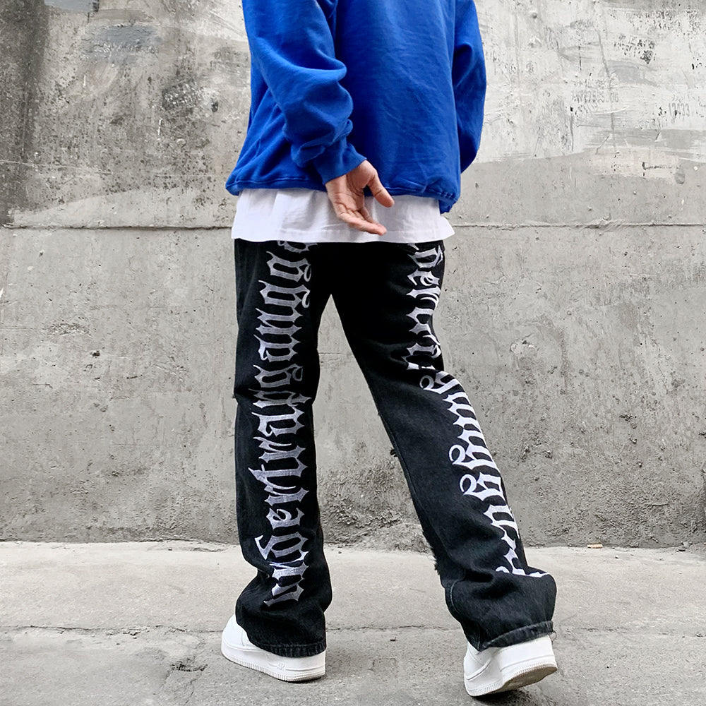 A man in Maramalive™ Hip Hop Vibe Back Gothic Alphabet Embroidery Ripped Micro Flared Denim Pants.