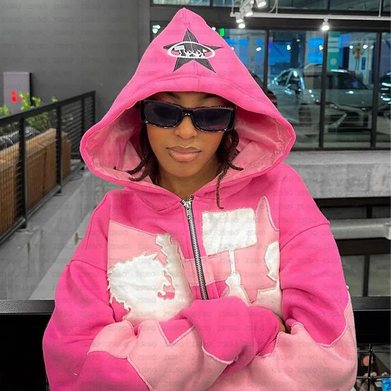 A person wearing a casual sweatshirt, specifically a pink Maramalive™ Y2k American High Street Trend Jacket Men Creative Embroidered Zipper Hoodie Harajuku Fashion Retro Oversized Sweatshirt Women with a star emblem on the hood and sunglasses, stands indoors with arms crossed.