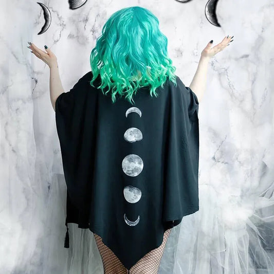 Person with turquoise hair, wearing a Maramalive™ Gothic Black Retro Moon Print Tassel Cloak Female Autumn and Winter Dark V-neck Loose Top Bat Cloak Goth Jacket Women, facing a gray marbled background, with their arms slightly raised.