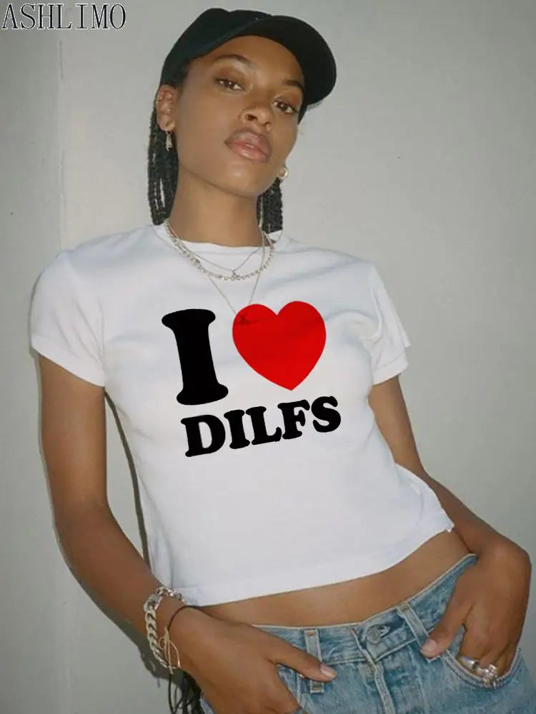 A person sporting a black cap and a Maramalive™ brand white T-shirt with the text "I ❤️ DILFS" stands against a plain wall, showcasing 2000s I Love Dilfs Women T-shirt Summer Clothing women Crop Tops Slim Goth Short Sleeve letter T-shirts Y2K Fashion perfect for summer.