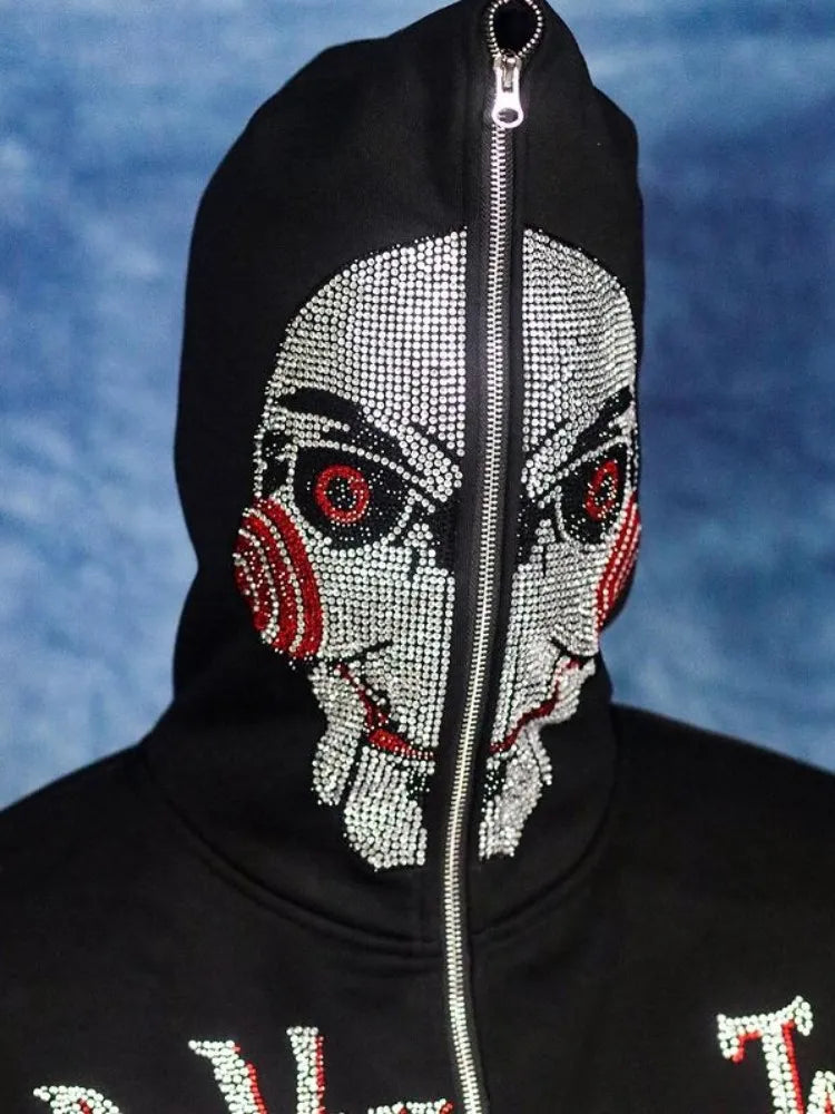 A person is wearing a black hooded jacket with a zipper, perfect for autumn and winter. This Maramalive™ Men Y2K Fashion Hoodie Letter Pattern Rhinestones Hoodie Clothes Hoodies Goth Grunge Long Sleeve Women Sweatshirt Oversized Tops features a mask design resembling a character with red spiral cheeks and a white face. The background is blue.