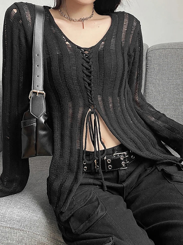 A person is seated on a couch, embodying gothic fashion with a black Maramalive™ Goth Dark Mall Gothic See Through Bandage Blouse Grunge Black Casual Sexy Knitwear T-shirt Y2k Long Sleeve Streetwear Women Tops and black cargo pants cinched with a belt. A black shoulder bag rests beside them.
