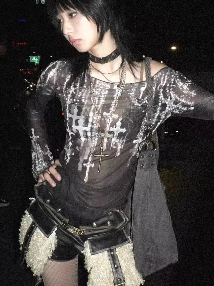A person stands with one hand on their hip, wearing a Maramalive™ Gothic Goth Black Mesh Tops Women Grunge Aesthetic Off Shoulder Graphic Crop T Shirts See Through Trashy Y2k 2000s Tees, leather shorts with large pockets, and several necklaces, including a cross. The slim fit ensemble embodies streetwear style against a dark background with some lights visible.