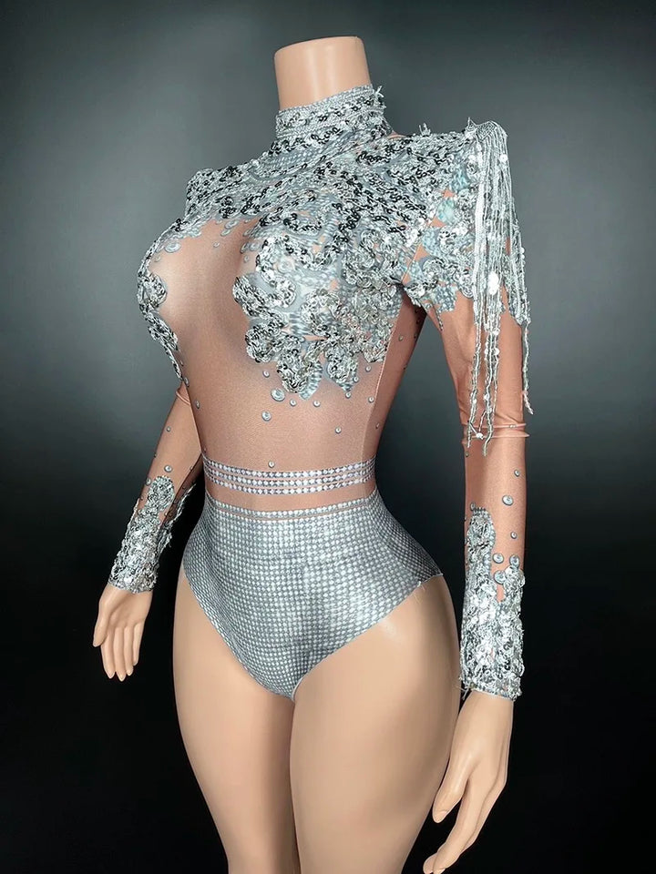 A mannequin dressed in a Maramalive™ Flashing Silver Sequins Fringe Spandex Bodysuit Women Dancer Singer Performance Costume High-Neck Long Sleeve Nightclub Stage Wear, adorned with intricate silver embellishments and transparent mesh sections, exuding a sexy club style vibe, posed against a plain dark background.