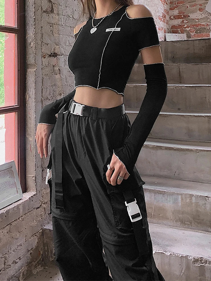 A person wearing a Maramalive™ Goth Dark E-girl Style Patchwork Black T-shirts Gothic Open Shoulder Sleeve Y2k Crop Tops Ruffles Hem Hip Hop Techwear Women Tee and black cargo pants with white accents stands indoors near a window and a staircase, showcasing a perfect blend of Gothic Casual Streetwear style.