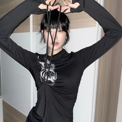 A person in a black long-sleeve top with a hand-painted pattern holds black strings near their face, standing in front of a light-colored background. The grunge style of the design adds an edgy touch to the Maramalive™ Grunge Irregular Tops Dark Aesthetics Bandage T-shirt Mall Goth Y2k Tight Tops Alternative Streetwear Fashion Emo.