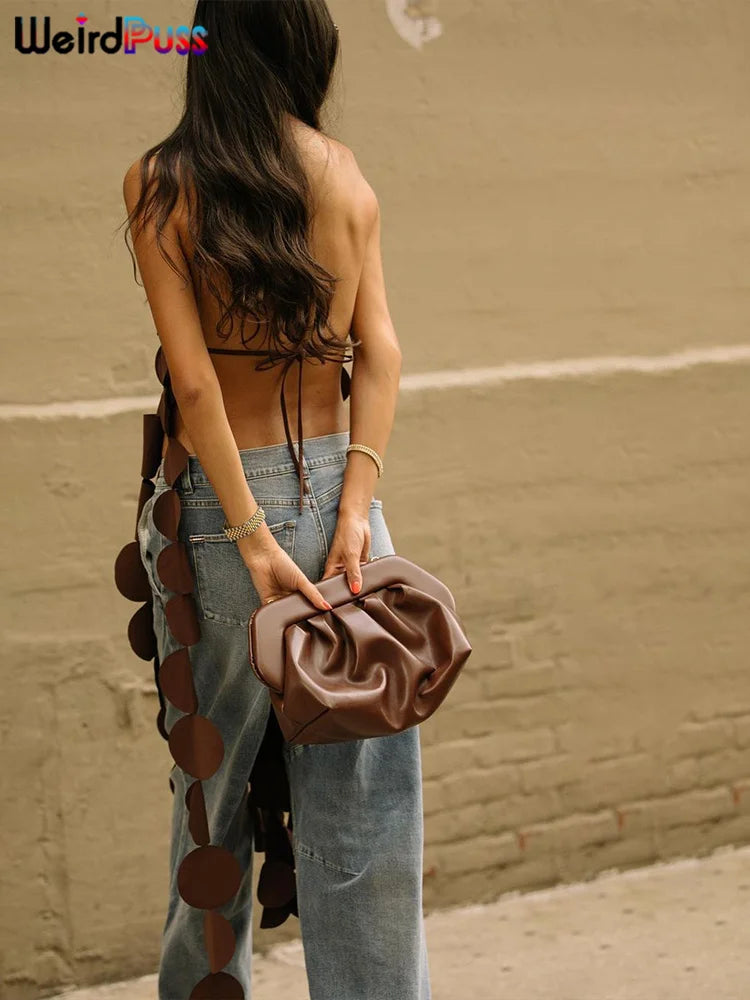 A woman with long, dark hair is seen from behind, wearing a Maramalive™ Irregular Tassel Halter Camisole Women Backless Bandage Sexy Chic Circle Beach Style Wild Stretch Midnight Clubw Vest and holding a brown clutch. She is walking along a street with a brick wall in the background.