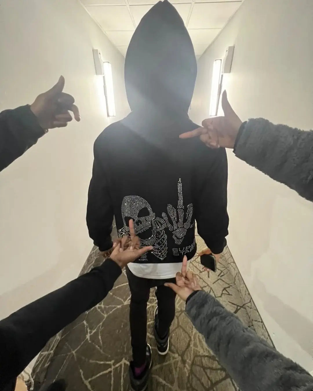 A person wearing a Maramalive™ Oversized Diamond Skull Print Streetwear Hoodie Vintage Streetwear Tops Sweatshirt Goth Hoodies Women Y2k Clothes, complete with a cozy cotton liner, is walking away while surrounded by multiple hands making a middle finger gesture.