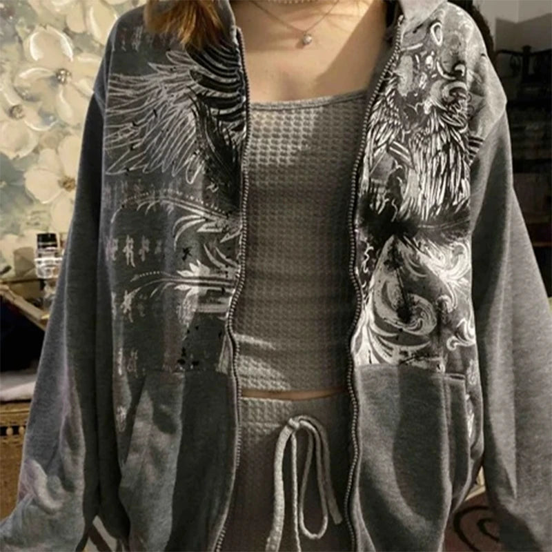 Person wearing a grey, geometric pattern Maramalive™ E-girl Gothic Dark Academia Sweatshirts Grunge Punk Letter Wings Graphic Zip Up Hoodie Y2K Aesthetic Mall Goth Coat over a grey knit top with a drawstring at the waist, standing indoors.