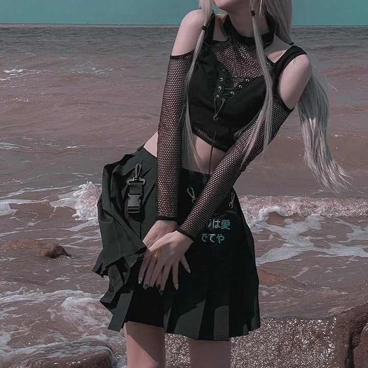 Person with long hair wearing a Maramalive™ Goth Dark Techwear Fishnet Open Shoulder Halter T-shirts Mall Gothic Grunge Black Bandage Crop Tops Women Punk Sexy Alt Clothing, waist cincher, and a skirt standing by the ocean, exuding Grunge Goth Punk vibes.