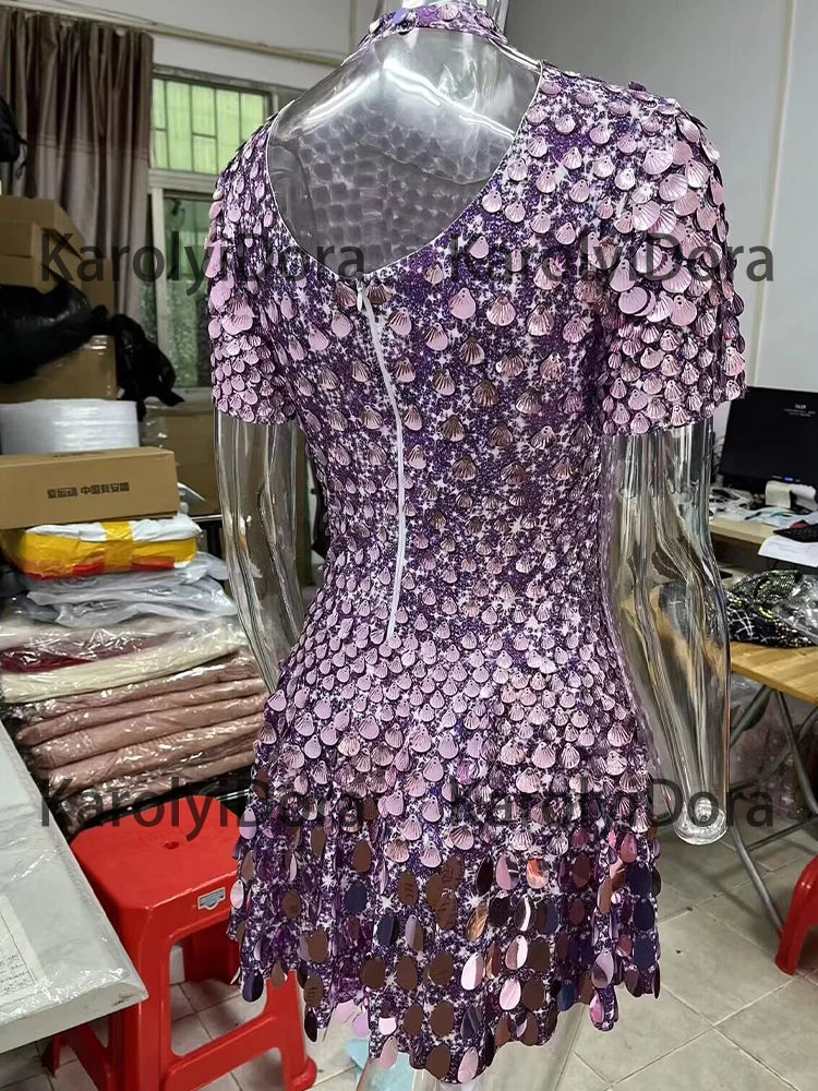 A shiny, purple sequined dress, reminiscent of a Dai Dance costume, is displayed on a transparent mannequin in a cluttered room with sewing supplies and machinery.

becomes

A Sexy Black Shell Sequins Mini Dress Nightclub Dance High Quality Performance Clothing Bodysuit Birthday Red Dress by Maramalive™ is displayed on a transparent mannequin in a cluttered room with sewing supplies and machinery.