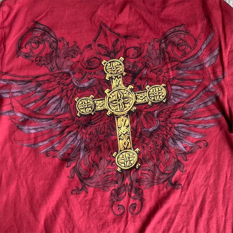 Close-up of a red fabric with an ornate gold cross design, featuring intricate detailing and flanked by faint dark wings and scroll patterns in the background, reminiscent of Maramalive™ 2000s Retro Grunge Indie Mall Goth Tees Vintage Graphic Patchwork Long Sleeve T-shirt Y2K Aesthetic Emo Women Men Tops Clothes.