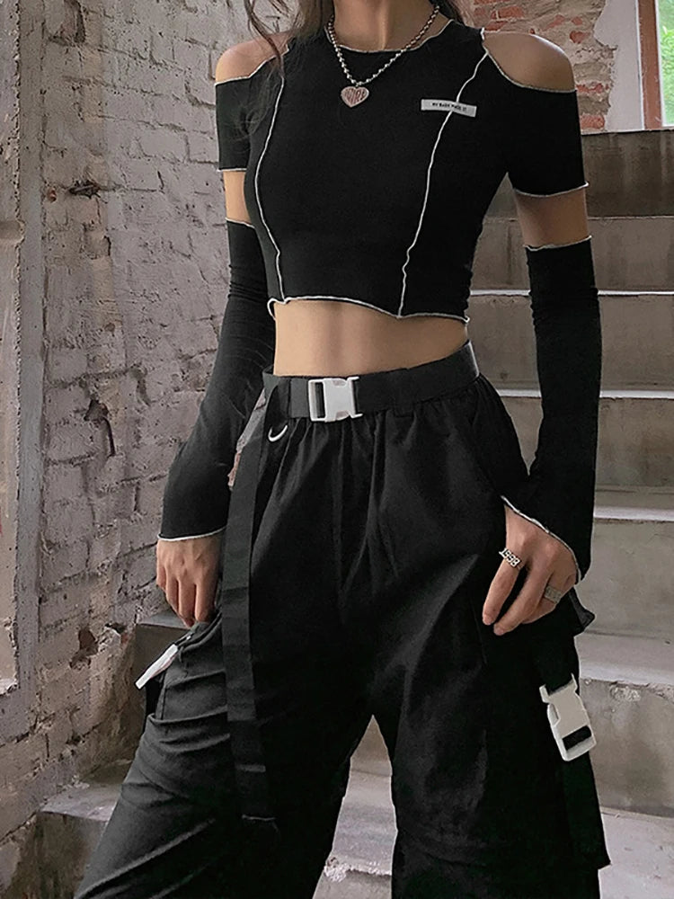 Person in a Maramalive™ Goth Dark E-girl Style Patchwork Black T-shirt Gothic Open Shoulder Sleeve Y2k Crop Top Ruffles Hem Hip Hop Techwear Women Tee and cargo pants with a white belt and accessories, embodying Gothic Casual Streetwear, stands in front of a brick wall and staircase.