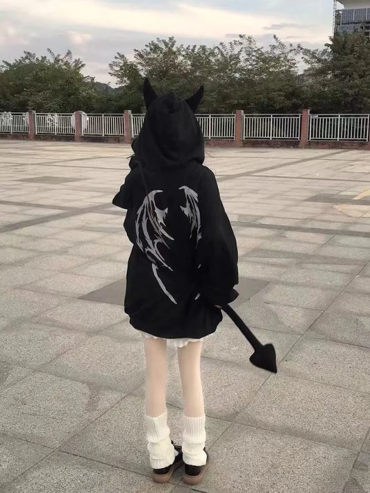 A person wearing a black hoodie with wing designs, white shorts, and white leg warmers stands on a paved area. The Maramalive™ Gothic Zip Up Hoodies Women Mall Goth Tops Streetwear Kawaii Hooded Sweatshirt 2022 Autumn Pullovers, embodying streetwear style with attached devil horns and a tail, makes a bold statement in women's fashion. Trees and railings are visible in the background.
