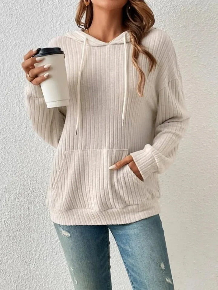 A lady in a beige ribbed hoodie and blue jeans holds a white takeaway coffee cup with one hand, while the other hand is in her "Maramalive™ Ladies Casual Knit Hoodie Sweatshirt Fall Winter Y2K Fashion Long Sleeve Women's Loose Hooded Sweater". This ensemble is perfect for Fall Winter Fashion.