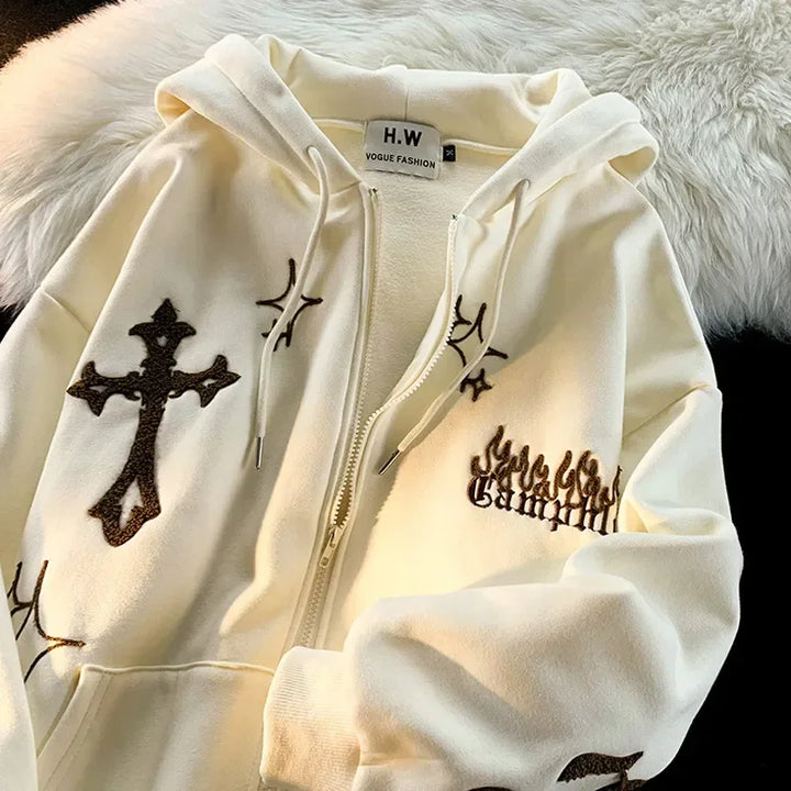 A cream-colored, oversized zip-up hoodie with a black cross design, Gothic text, and various other black embroidery patterns. This Embroidery Sweatshirt Women Oversized Zip-Up Hoodies Gothic Hip Hop Hooded Streetwear Female Hoodie Y2k Full Jacket by Maramalive™ exudes Gothic Hip Hop Streetwear vibes on a white furry surface.