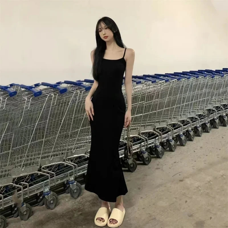 A woman in a long, black Maramalive™ Autumn Pure Sleeveless Dress Women Sexy Sheath Hotsweet Style Fashion All-match Vestido Feminino New Arrival Popular Chic and beige sandals stands in front of a row of empty shopping carts in a store or warehouse setting.