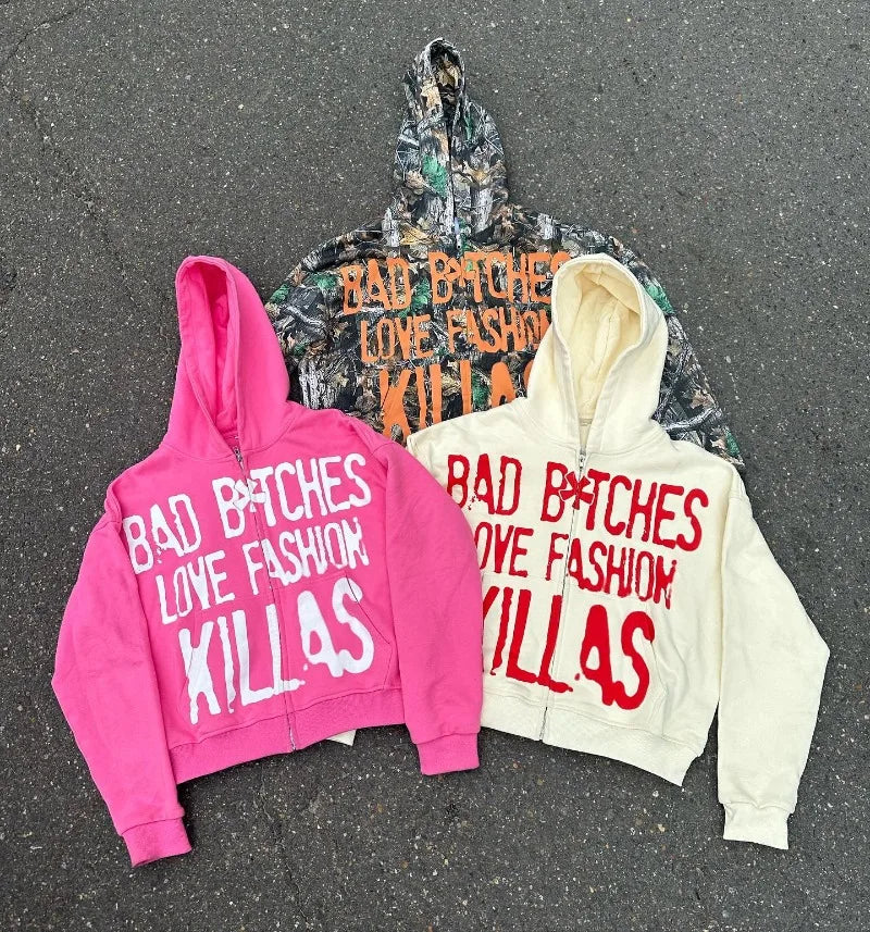 Three y2k Streetwear Goth Letter Print Oversized Hoodie Women 2024 Fashion Casual Loose Harajuku Versatile Zipper Sweatshirt Tops from Maramalive™ with the phrase "BAD B*TCHES LOVE FASHION KILLAS" in bold text. The hoodies, available in pink, camouflage, and cream colors, exude streetwear vibes as they are laid out on a pavement surface.