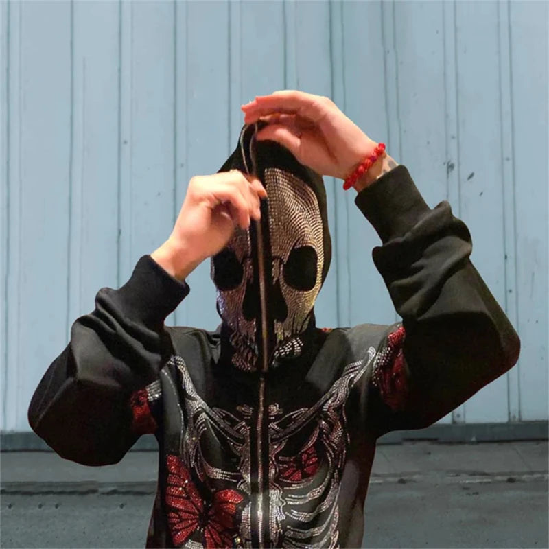 A person donning a black skull mask and a Maramalive™ Goth Clothing Rhinestones Skeleton jacket Hoodies Punk Long Sleeve Streetwear Oversized Zip Men Y2K Casual Hoodie Sweatshirt New with red designs is lifting the mask slightly. The background appears to be a plain wall, capturing the edgy essence perfect for spring and autumn.