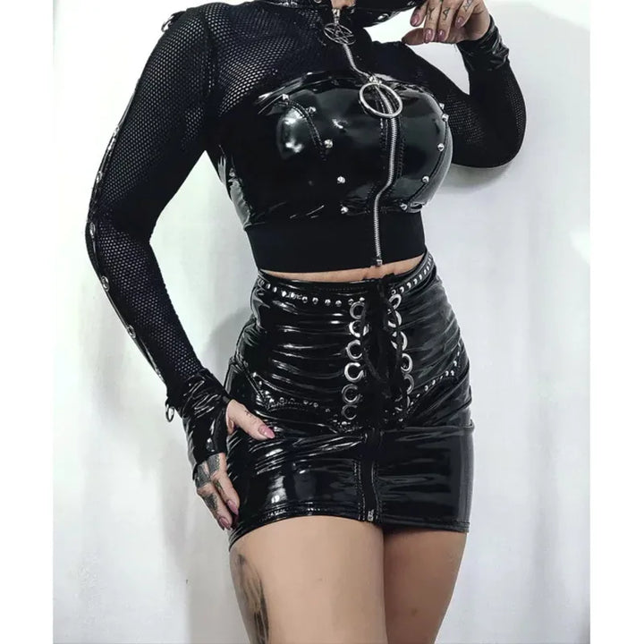 An individual in a Maramalive™ Goth Dark Grunge Punk Fishnet Zip Up Cardigans Mall Gothic Faux Pu Hooded Crop Jackets Women Sexy Streetwear Club Alt Smock Tops, featuring a zip-up top and laced-up shorts, stands against a white background, embodying gothic fashion.