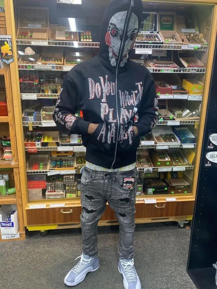 Person wearing a detailed mask and a black Men's Maramalive™ Y2K Fashion Hoodie Letter Pattern Rhinestones Hoodie Clothes Hoodies Goth Grunge Long Sleeve Women Sweatshirt Oversized Tops that reads "Do You Want To Play A Game?" standing in a store aisle with various small boxes on shelves in the background. The cozy fleece design makes it perfect for autumn and winter strolls.